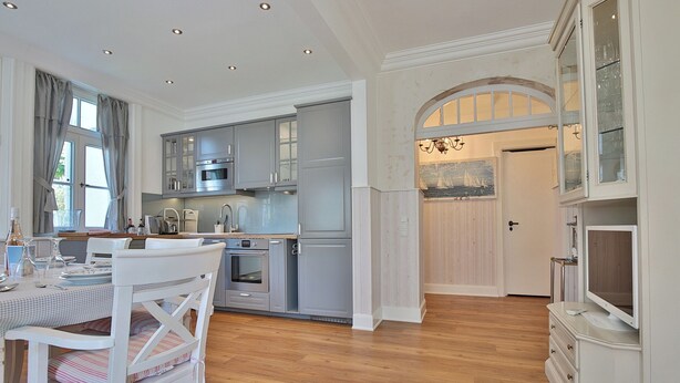 A modern kitchen with grey cabinets, a dining table with chairs, and a wooden floor. - Villa Schöneck Appartement 1 (Scharbeutz)