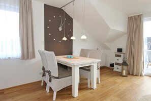 A dining area with a white table and chairs, a clock on the wall, pendant lights, and a view of the outdoors.