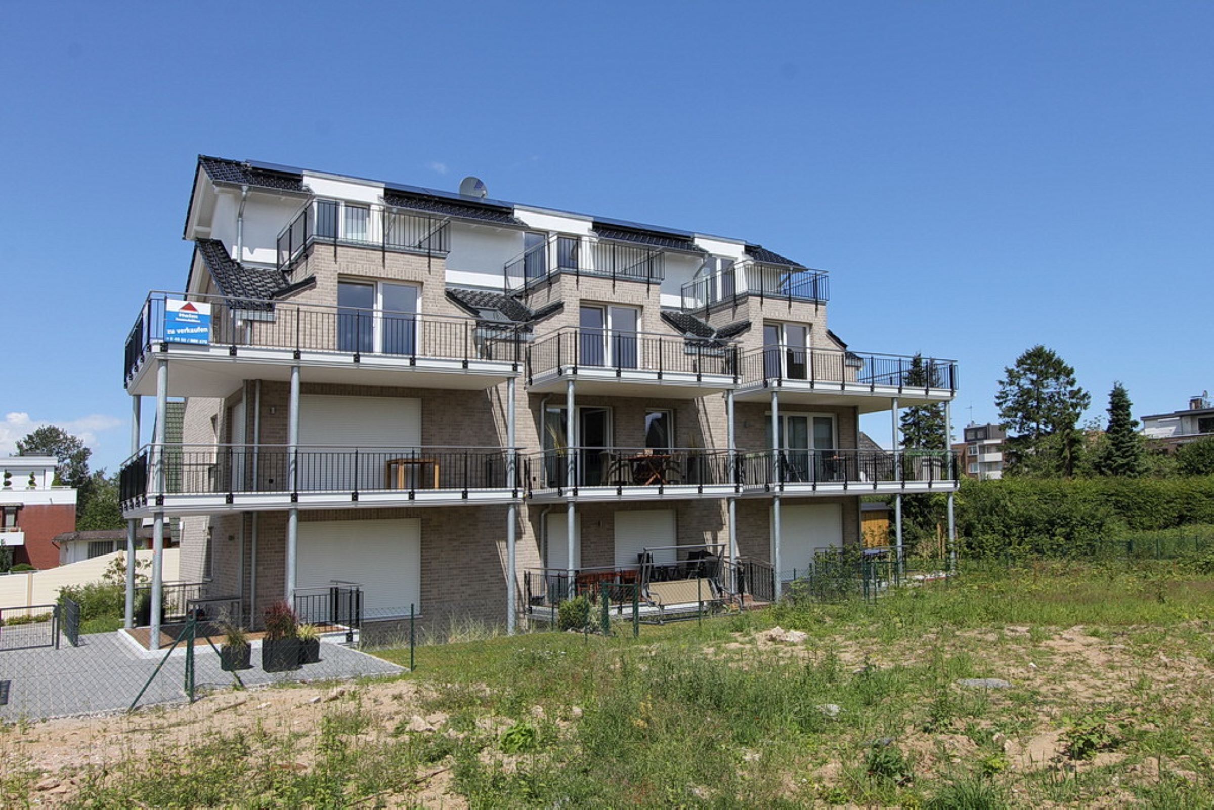 Un edificio residencial de varios pisos con balcones, un letrero visible y un área exterior cercada.