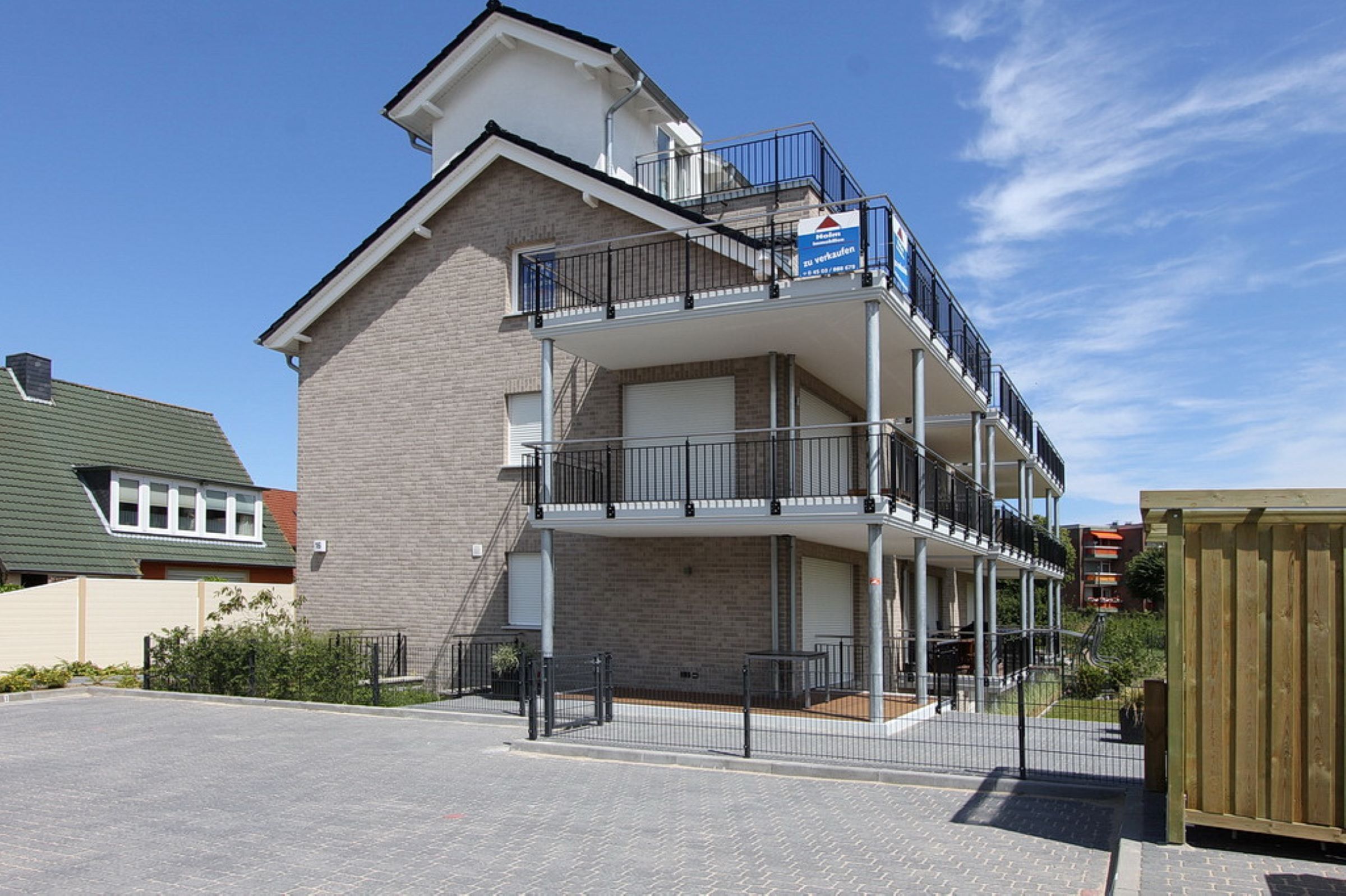 A two-story building with a balcony on the upper floor, a garage door on the ground floor, and a clear sky in the background.