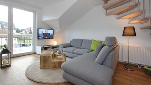 A modern living room with a grey sectional sofa, a wooden coffee table, a floor lamp, and a television on a white wall. - Domizil am Möwenberg Appartement 9 (Scharbeutz)