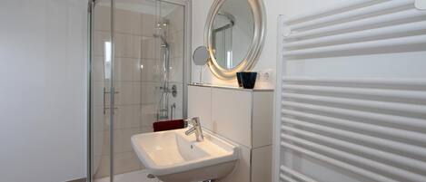 Un baño moderno con cabina de ducha de vidrio, un lavabo blanco y un espejo.