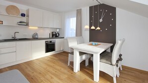 A modern kitchen with white cabinetry, a built-in oven, and a dining area with a white table and wicker chairs. - Domizil am Möwenberg Appartement 9 (Scharbeutz)