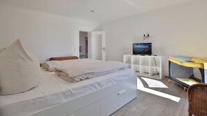 Un dormitorio con cama, televisión, armario blanco y una cuna.