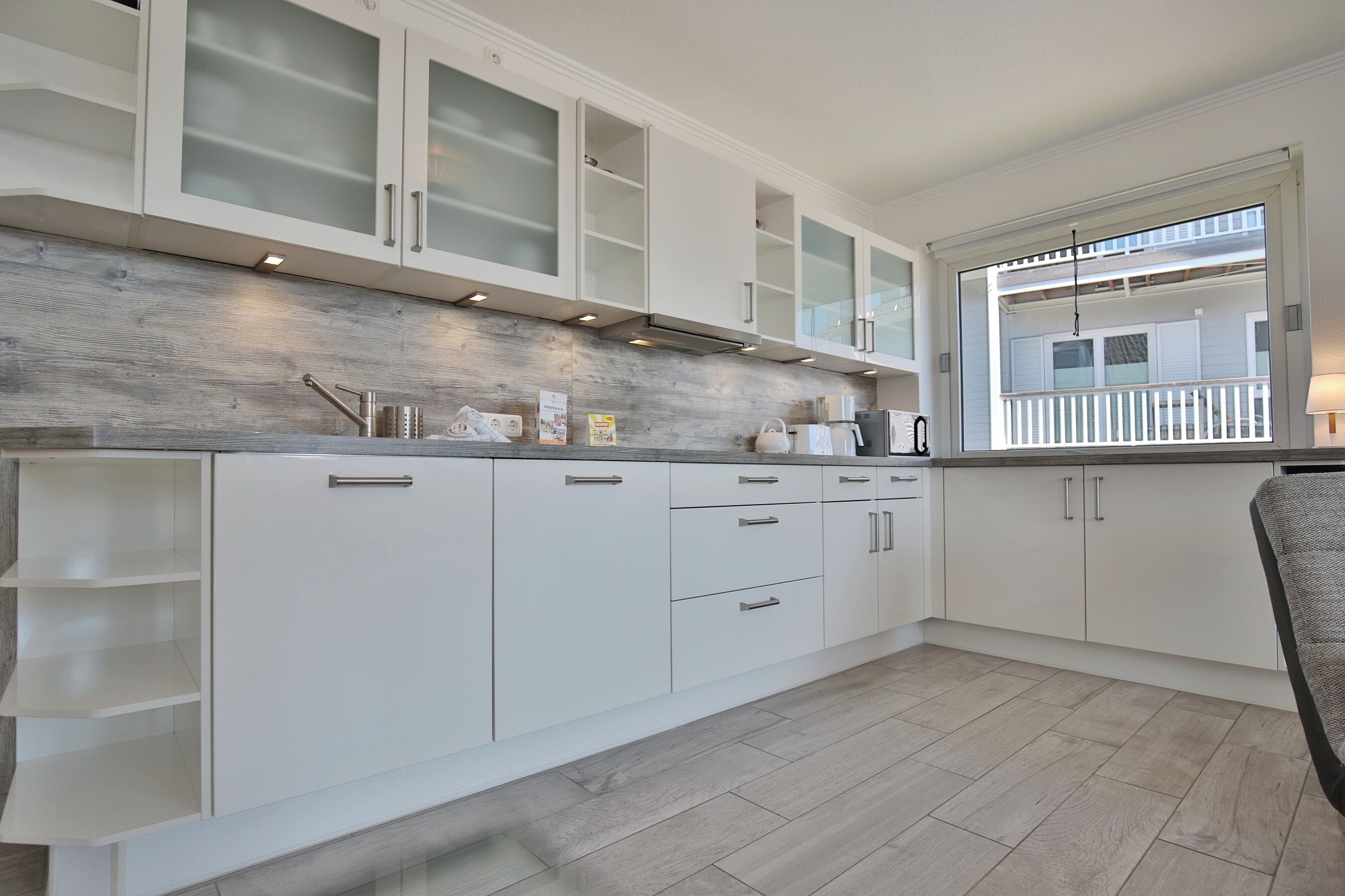 Een moderne keuken met witte kastjes, een houten spatwand en een raam met uitzicht op een balkon.