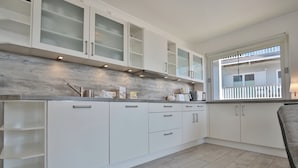 Una cocina moderna con armarios blancos, un salpicadero de madera y una ventana con vistas a un balcón.