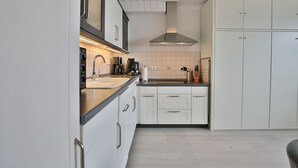 A modern kitchen with white cabinets, a stainless steel range hood, and a black coffee machine. - Seetempel Appartement 27 (Scharbeutz)