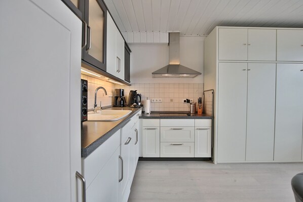 A modern kitchen with white cabinets, a stainless steel range hood, and a black coffee machine. - Seetempel Appartement 27 (Scharbeutz)