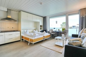 A modern hotel room with a kitchenette, two beds, a dining area, and a view of the sea. - Seetempel Appartement 27 (Scharbeutz)