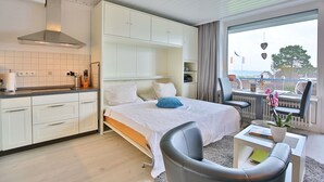 A modern hotel room with a bed, a desk, a chair, a small table, and a view of the sea. - Seetempel Appartement 27 (Scharbeutz)