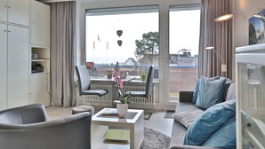 A modern living room with a sofa, chairs, a coffee table, and a view through large windows. - Seetempel Appartement 27 (Scharbeutz)