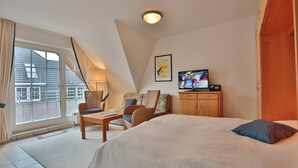 A hotel room with a bed, a TV, a sofa, a chair, a table, and a window with curtains. - Parkblick Appartement 11 (Scharbeutz)