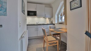 A compact kitchen with white cabinets, a microwave, and a dining area with a table and chairs. - Parkblick Appartement 11 (Scharbeutz)