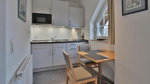 A compact kitchen with white cabinets, a microwave, and a window providing natural light. - Parkblick Appartement 11 (Scharbeutz)