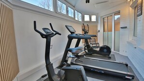 Une salle de sport à domicile équipée d’appareils de cardio, notamment un vélo d’appartement, un vélo elliptique et un tapis de course.