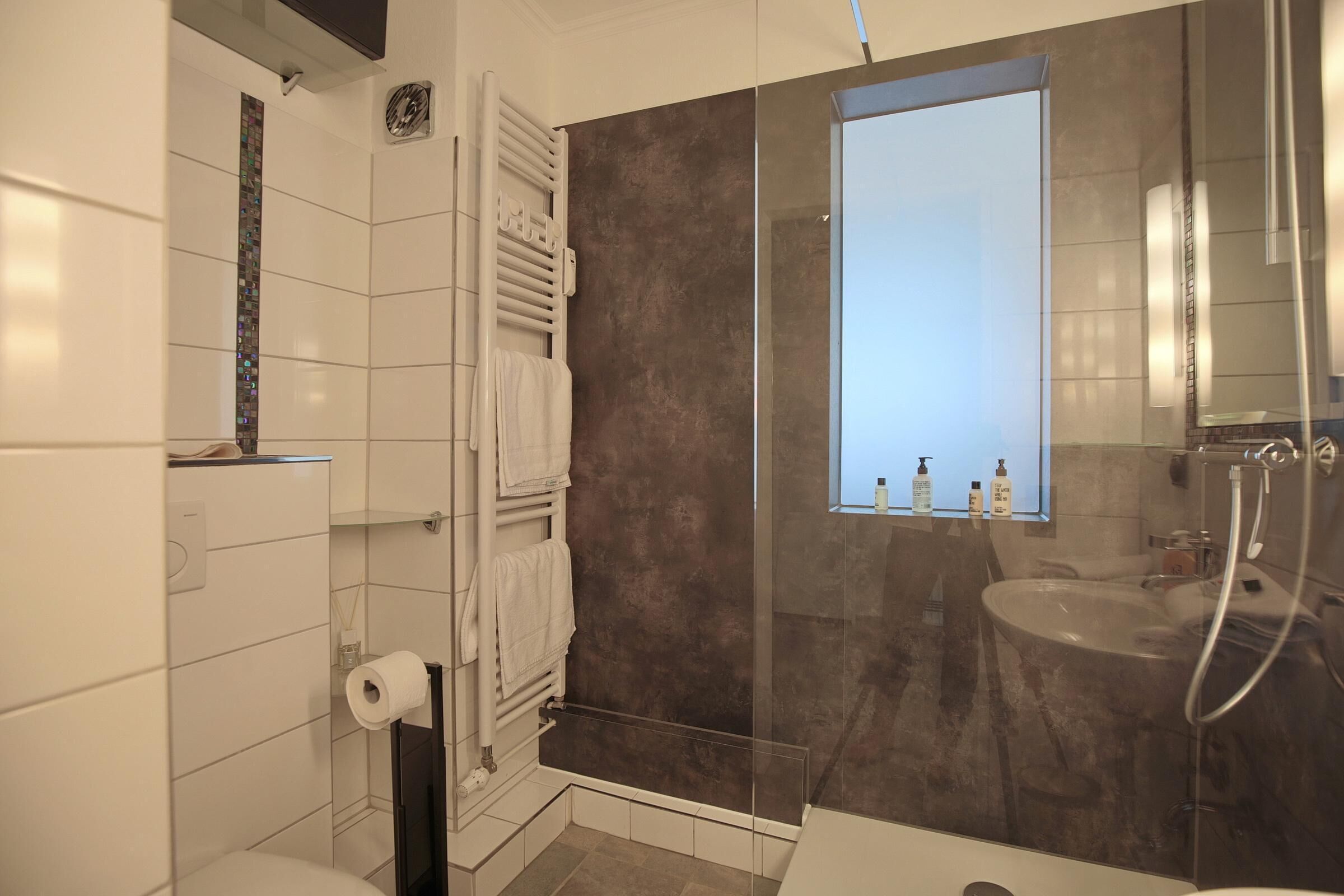 Et moderne badeværelse med en glasbrusekabine, toilet og vask med spejl.