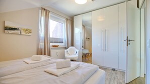Quarto de hotel com duas camas, um guarda-roupa espaçoso, uma cadeira e uma janela com cortinas.