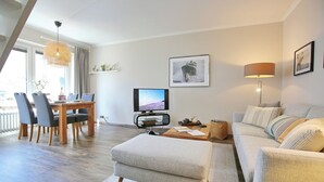 Uma sala de estar moderna com área de jantar, sofá, televisão e luminária.