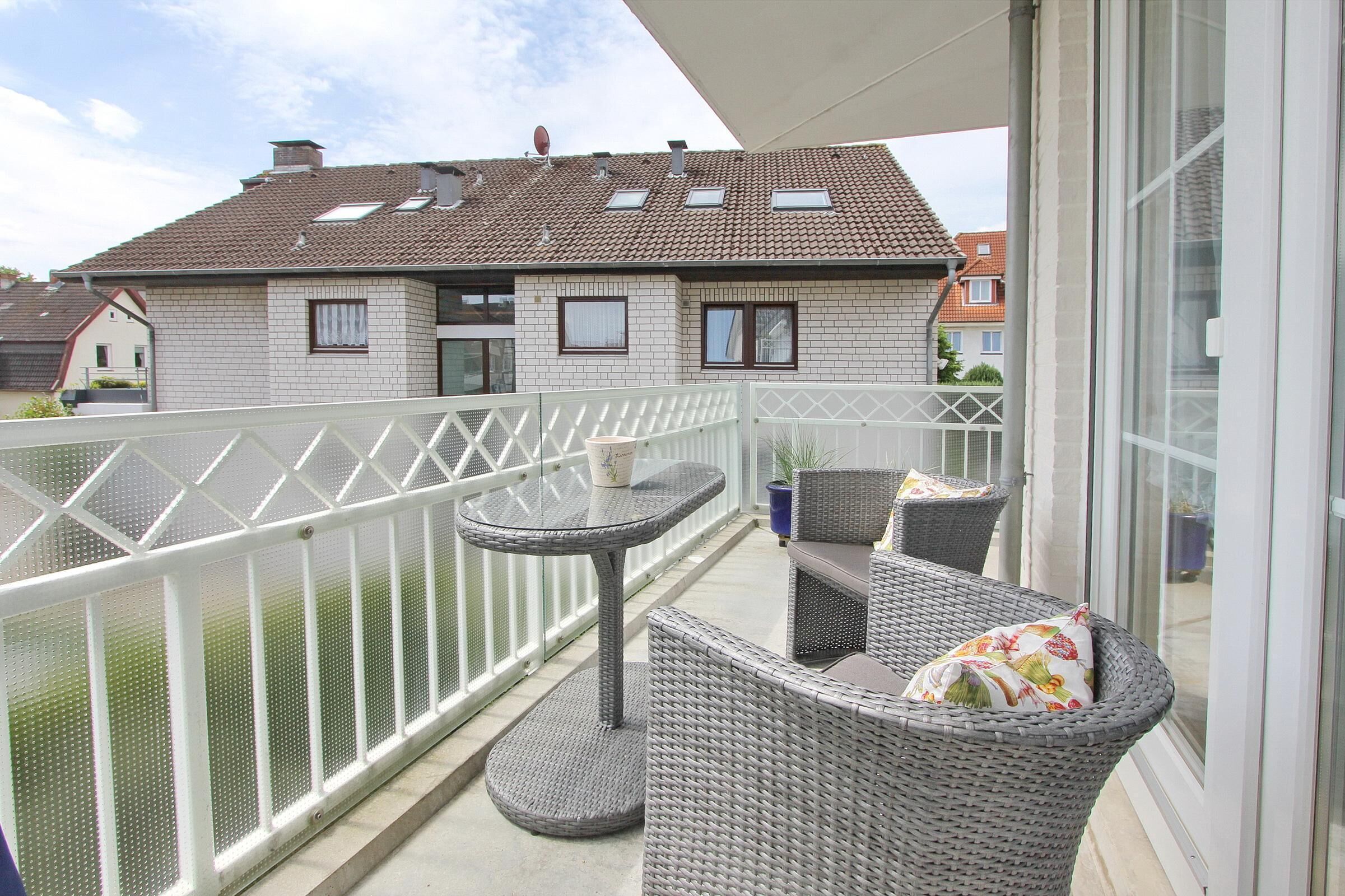 A balcony with wicker furniture and a table, overlooking a residential area.