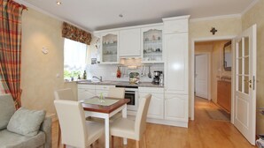 Une cuisine compacte avec des meubles blancs, un coin repas comprenant une table et des chaises, et un four visible.