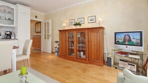 Un salon moderne avec un meuble en bois, une table basse en verre, un téléviseur et, au fond, un coin cuisine.