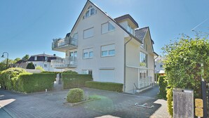 Un immeuble résidentiel de deux étages doté d’un balcon, d’un petit jardin et d’une allée pavée.