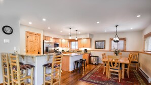Une cuisine moderne avec des meubles en bois, un îlot central, des tabourets de bar et un coin repas agrémenté d’un tapis.