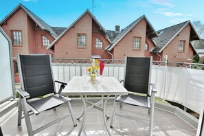 Une terrasse avec deux chaises et une table, une clôture blanche et une maison en briques en arrière-plan.