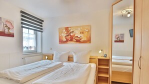 A bedroom with two beds, a painting on the wall, a window with blinds, and a bedside table with a lamp. - Residenz Alte Bergstrasse Appartement 9 (Scharbeutz)