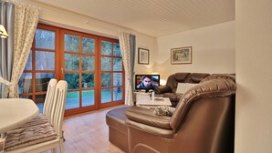 A living room with a brown leather sofa, a white dining table with striped cushions, and a television on a white table. - Ferienparadies Klingberg Appartement 5 (Scharbeutz-Klingberg)
