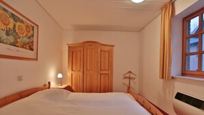A bedroom with a wooden bed, a wardrobe, a bedside lamp, and a window with curtains. - Ferienparadies Klingberg Appartement 5 (Scharbeutz-Klingberg)