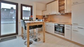 A modern kitchen with a wooden table, bar stools, a built-in oven, and white cabinets.