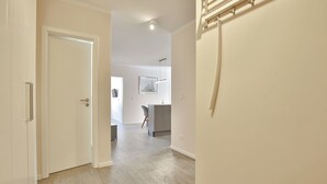 Un passadís amb sòl de fusta, una porta blanca i una escala que porta a una planta.