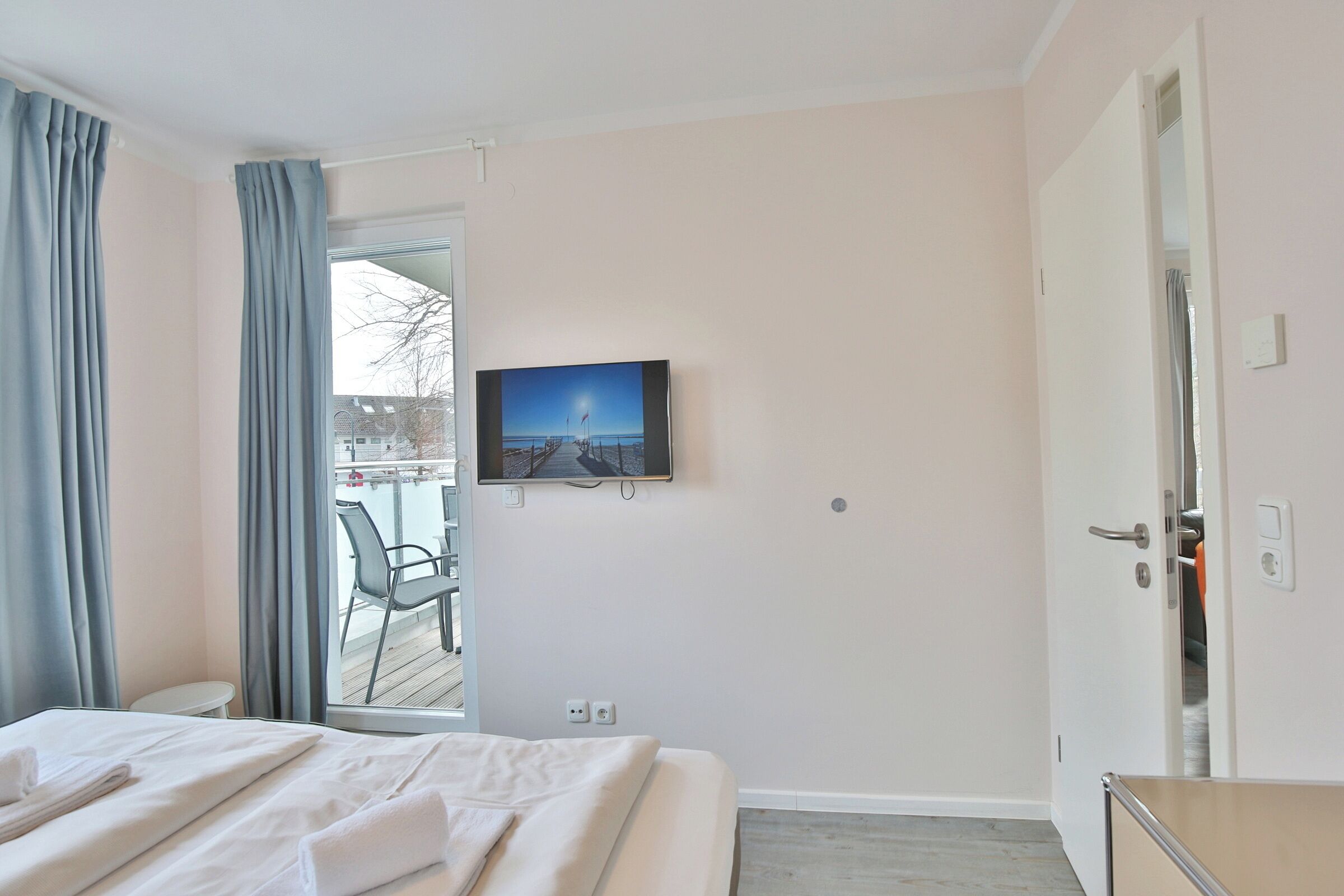 A hotel room with a bed, a television mounted on the wall, and a view of the outside balcony.
