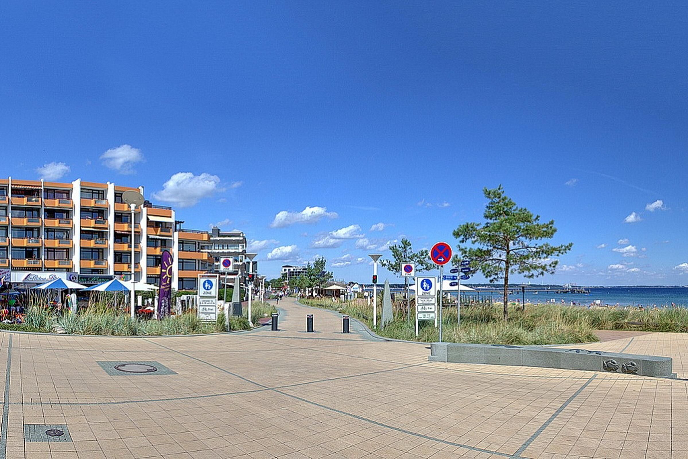A beachfront promenade with a modern hotel, clear skies, and a view of the sea.