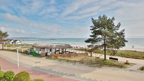 A beachside restaurant with outdoor seating, a thatched-roof structure, and a view of the sea. - Berliner Hof Apartment 215 (Scharbeutz)
