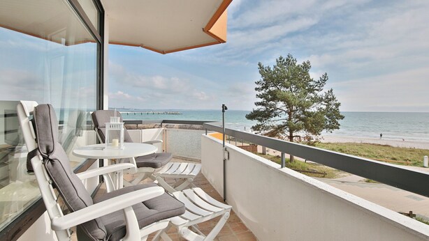 A balcony with white chairs and a small table, overlooking a beach and the sea. - Berliner Hof Apartment 215 (Scharbeutz)