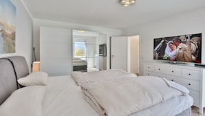 Et moderne soveværelse med en stor seng, fjernsyn og et garderobeskab.