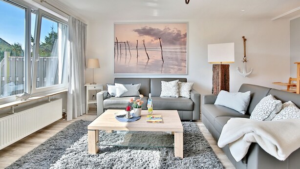 A modern living room with a grey sofa, a wooden coffee table, and a large window. - Appartementhaus Linda-lu Appartement 3 (Scharbeutz)
