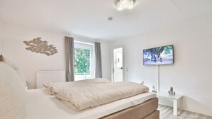 A bedroom with a bed, a window, a TV, and a view of the outdoors. - Appartementhaus Linda-lu Appartement 3 (Scharbeutz)