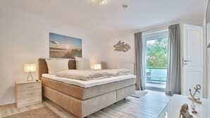 A bedroom with a large bed, bedside tables, a nightstand, a desk, and a view of the outdoors. - Appartementhaus Linda-lu Appartement 3 (Scharbeutz)