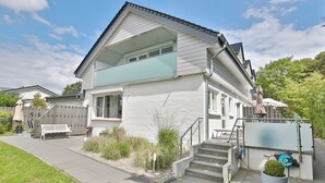 A modern two-story house with a balcony, a front porch, and a small garden area. - Appartementhaus Linda-lu Appartement 3 (Scharbeutz)