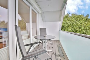 A balcony with a glass railing, a round table, and two chairs.