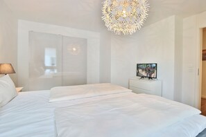 A modern bedroom with a large bed, a TV on a stand, and a unique chandelier. - Haus Meeresbrise Appartement 16 (Haffkrug)