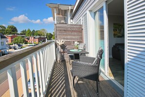A balcony with a table and chairs, a railing, and a view of the street and buildings. - Haus Meeresbrise Appartement 16 (Haffkrug)