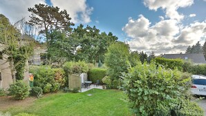 Een verzorgde tuin met gazon, een klein terras met tafel en stoelen, en diverse struiken en bomen.