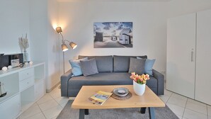 Een moderne woonkamer met een grijze bank, een houten salontafel, een witte kast en een schilderij aan de muur.