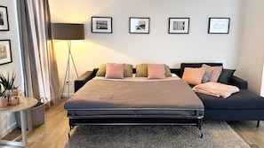 A modern bedroom with a bed, a sofa, and a floor lamp. There are framed pictures on the wall. - Haus Meeresbrise Appartement 19 (Haffkrug)