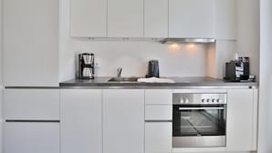 Une cuisine moderne avec des meubles blancs, un four en acier inoxydable, une machine à café et une bouilloire.