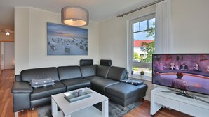 Een moderne woonkamer met een hoekbank, een flatscreen-tv en een schilderij van een strand.